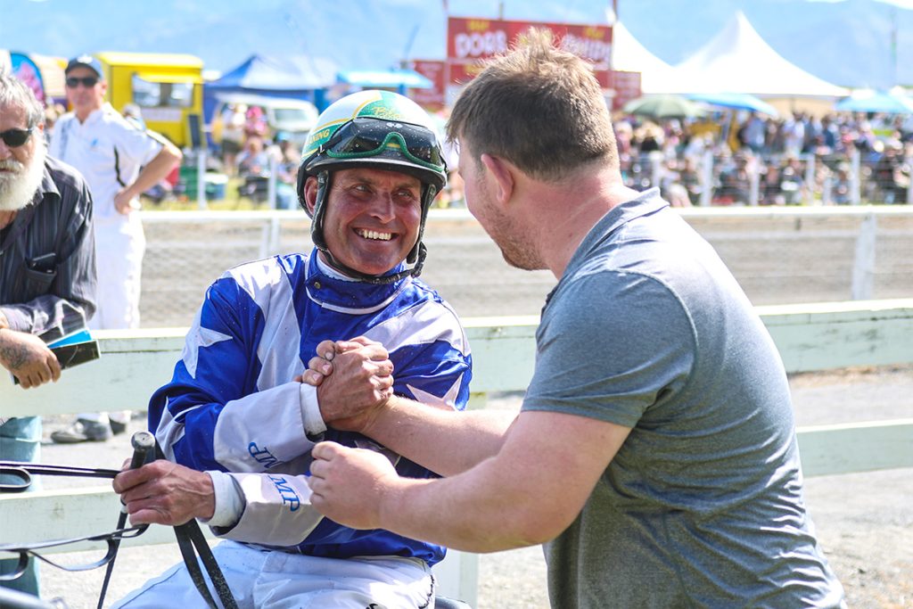 Blair Orange in blue and white silks smiling and shaking hands with Michael Purdon at Kaikoura Raceway.